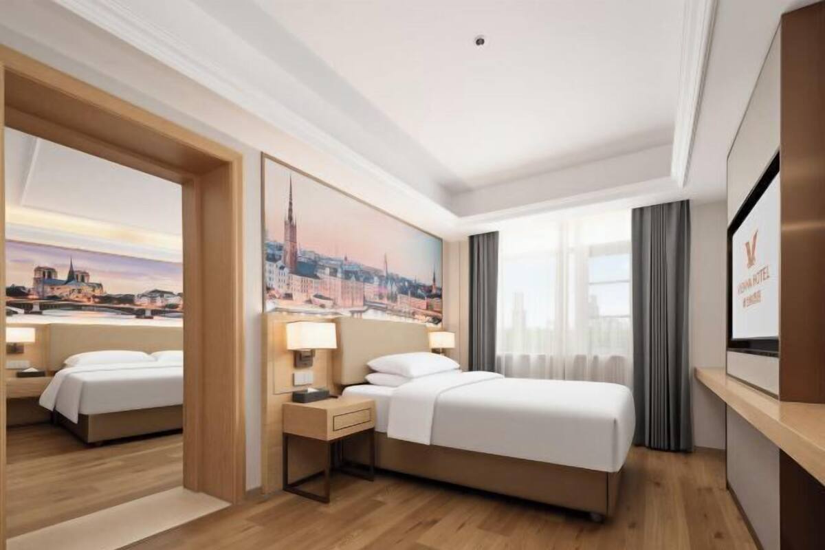A hotel room with a bed, bedside tables, a TV, and a cityscape painting on the wall.