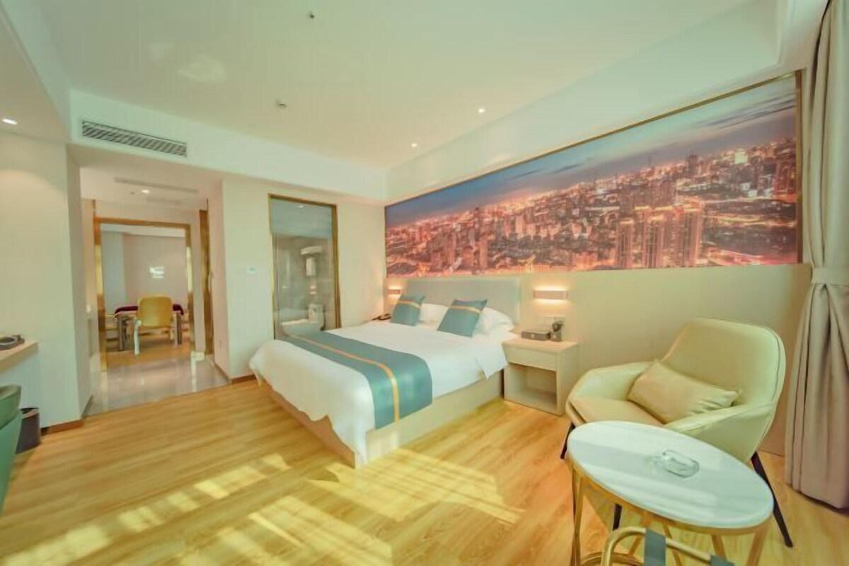 A hotel room with a large bed, a chair, a small table, and a cityscape view.
