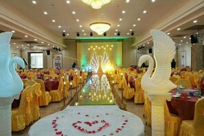 A banquet hall with rows of tables, a central stage with a backdrop, and large decorative swan sculptures.