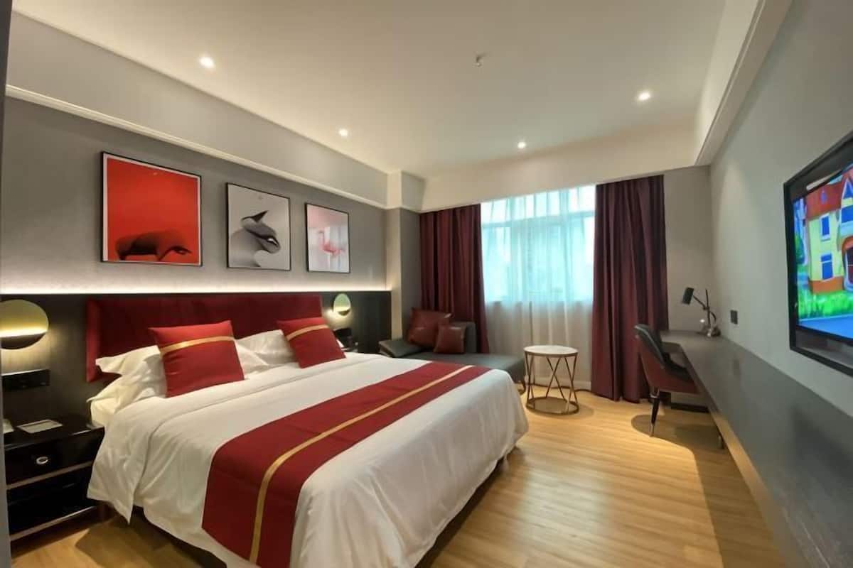 Habitación de hotel con una cama grande, un escritorio, una silla, un televisor y una ventana con cortinas.
