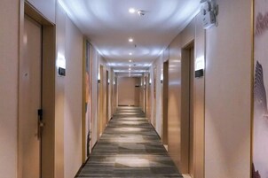 Un pasillo de hotel con puertas a ambos lados, suelo alfombrado e iluminación en el techo.