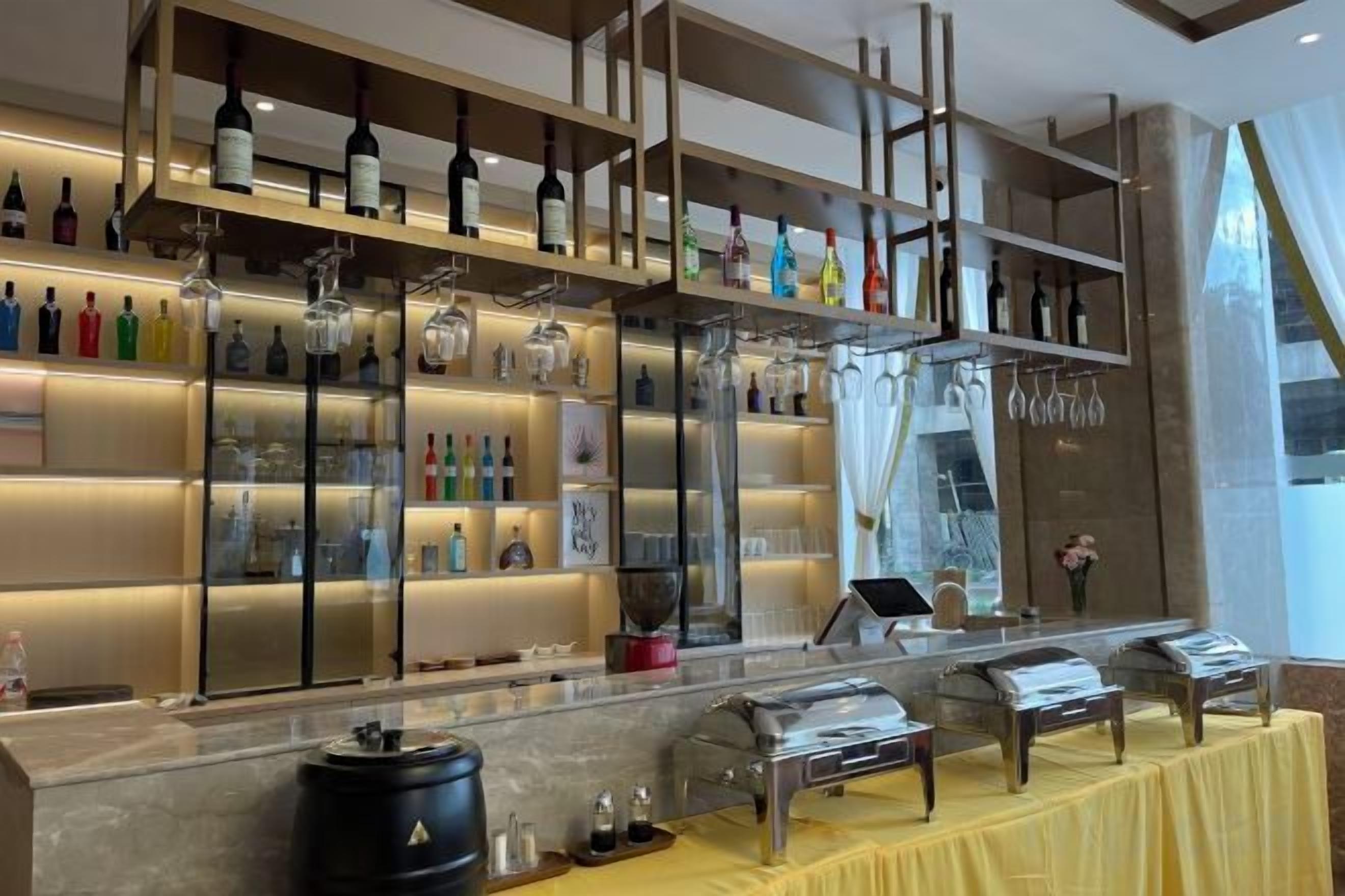 A bar area with shelves of bottles, a cash register, and a yellow tablecloth.