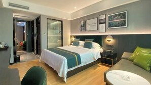 Una habitación de hotel moderna con una cama grande, un escritorio y una silla. Hay cuadros en la pared y una mesita de noche con una lámpara.