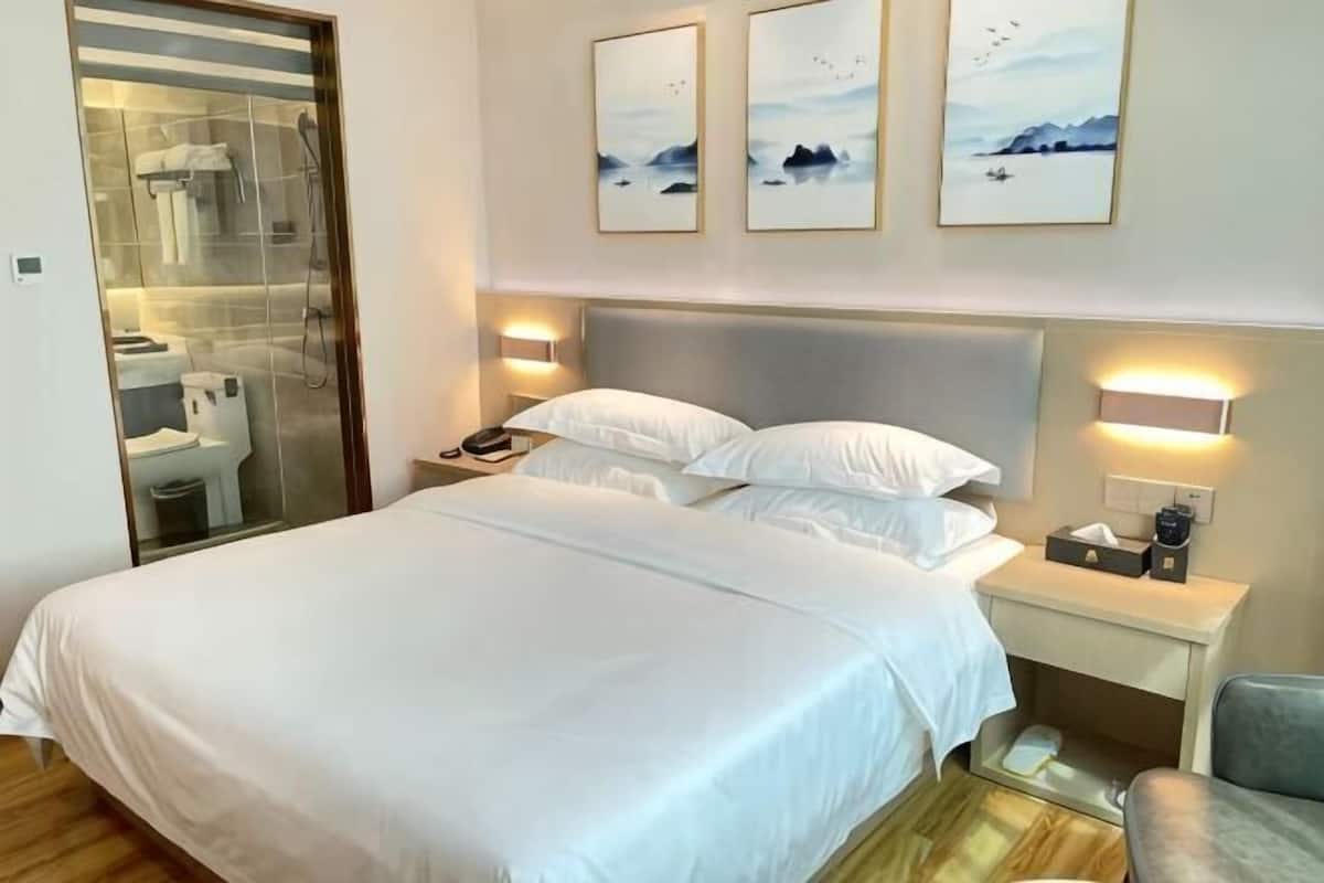Una habitación de hotel con cama, mesita de noche, lámpara y una obra de arte en la pared.