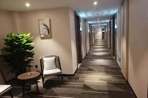 Un pasillo de hotel con alfombra estampada, una silla, una mesa y una planta en maceta.