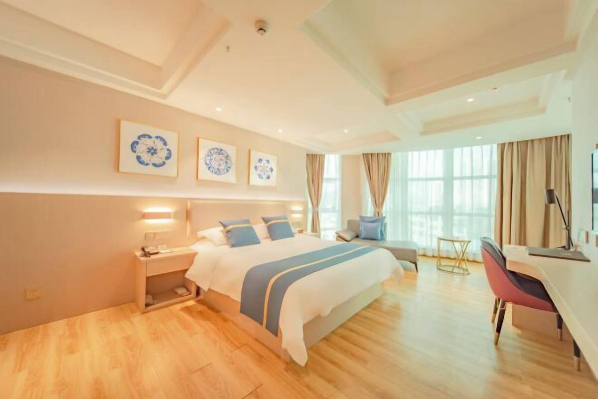Habitación de hotel con cama, mesita de noche, escritorio, silla y ventanas amplias.
