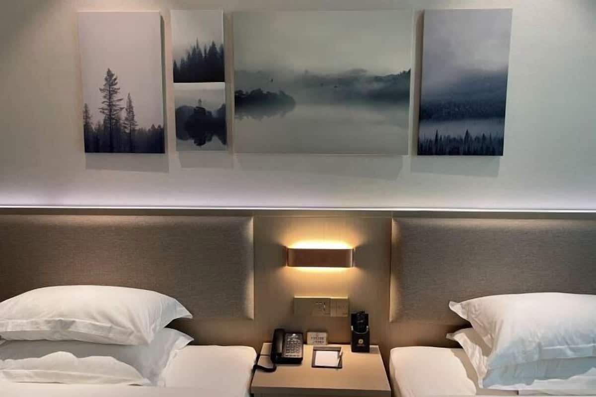 Habitación de hotel con dos camas, una mesita de noche con lámpara, teléfono y una obra de arte en la pared.