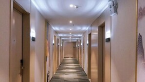 Un largo y estrecho pasillo de hotel con puertas a ambos lados, iluminación empotrada y suelo estampado.
