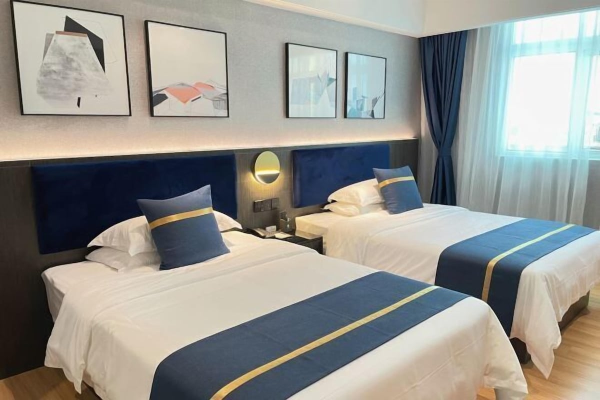 Quarto de hotel com duas camas, cada uma com colcha e almofadas azuis e brancas. Quadros emoldurados na parede acima das camas.