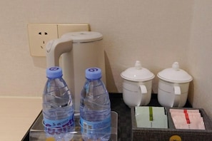 Quarto de hotel com minibar contendo duas garrafas de água, uma máquina de café, duas bules de chá brancos e uma bandeja com sachês de chá.