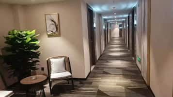 A hotel corridor with a carpeted floor, a chair, a table, and a potted plant.