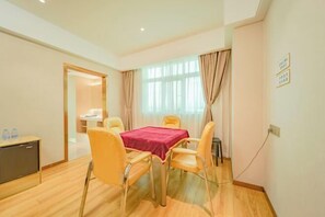 A hotel room with a dining table, chairs, a TV, and a window with curtains.