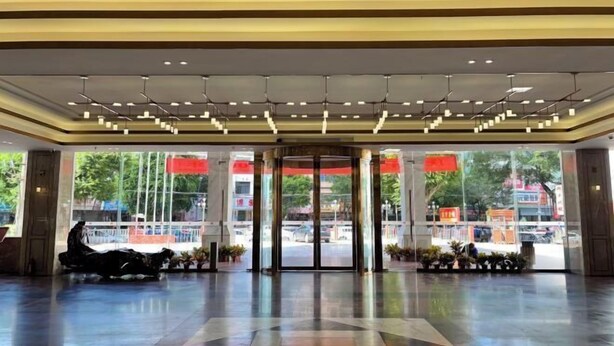 Un vestíbulo espacioso con un diseño moderno de techo, grandes puertas de vidrio que dan al exterior y una zona de estar con algunas sillas.