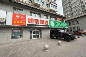 A hotel with a signboard, a parked SUV, and a building facade.