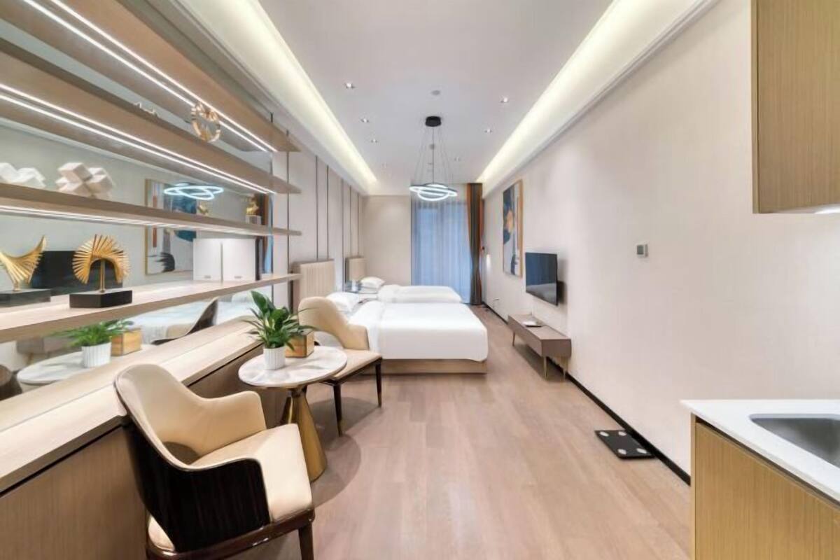 A modern hotel room with a bed, bedside table, chair, and a small dining area.
