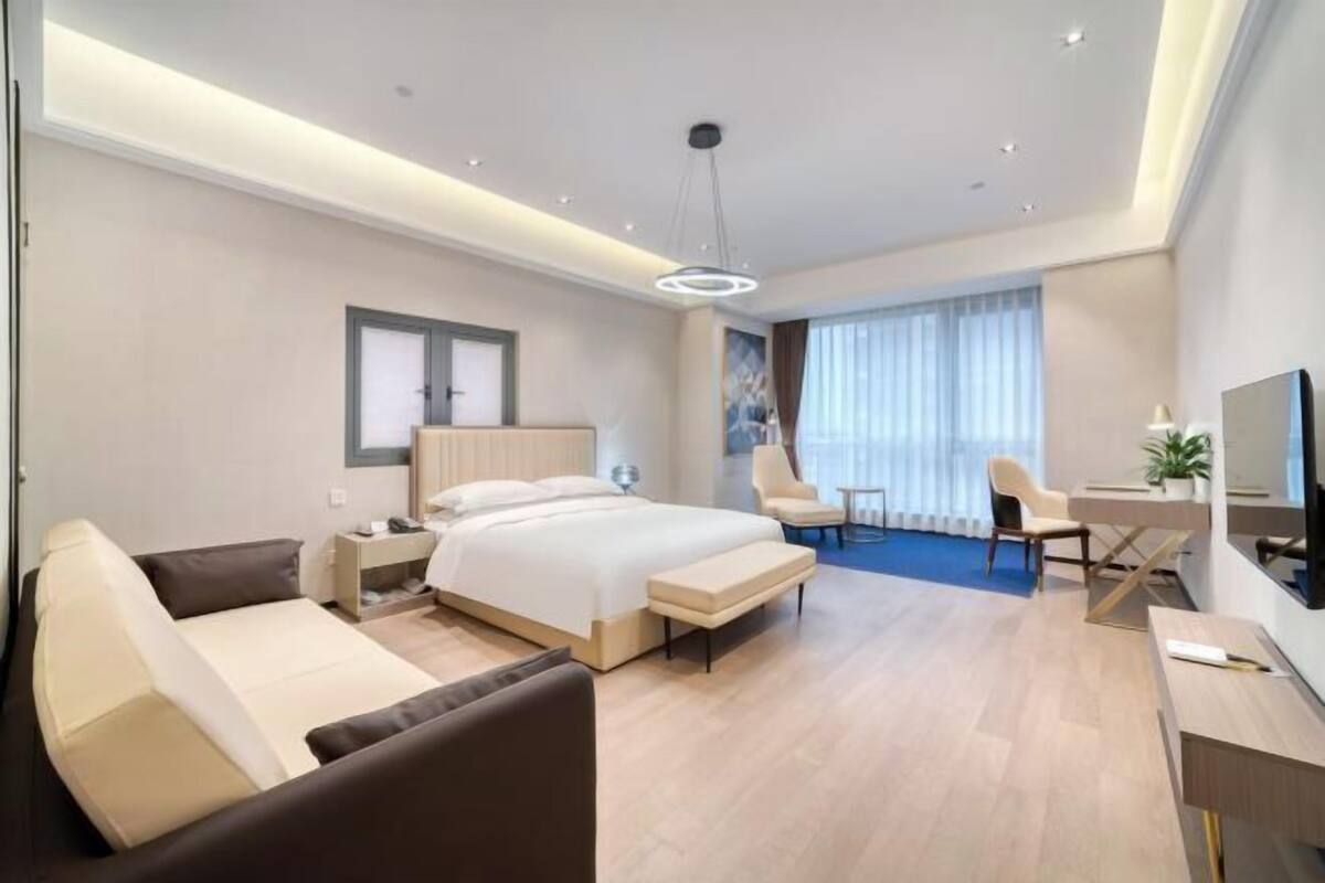 A modern hotel room with a large bed, a sofa, a desk, and a TV.