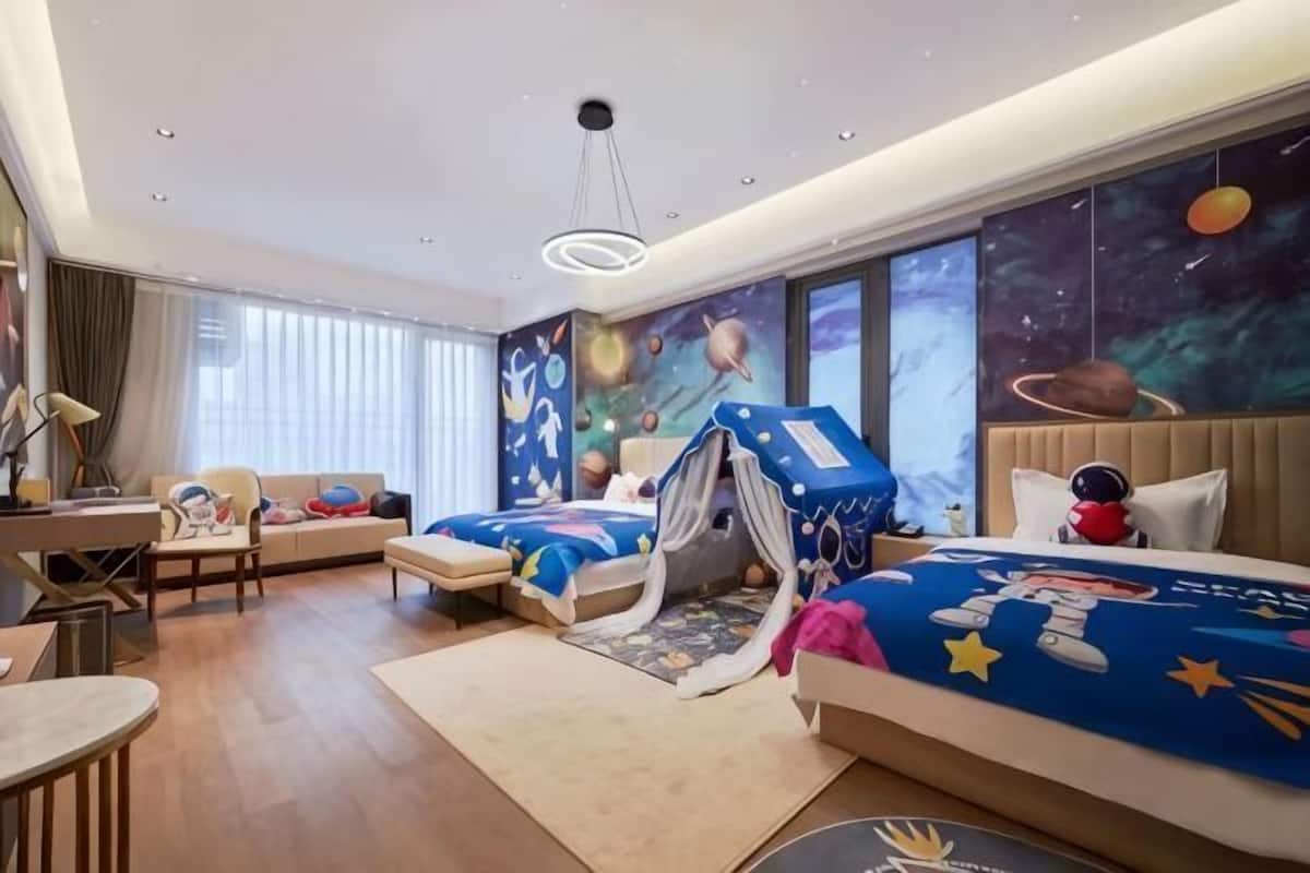 A hotel room with two beds, a desk, a chair, and a large window.