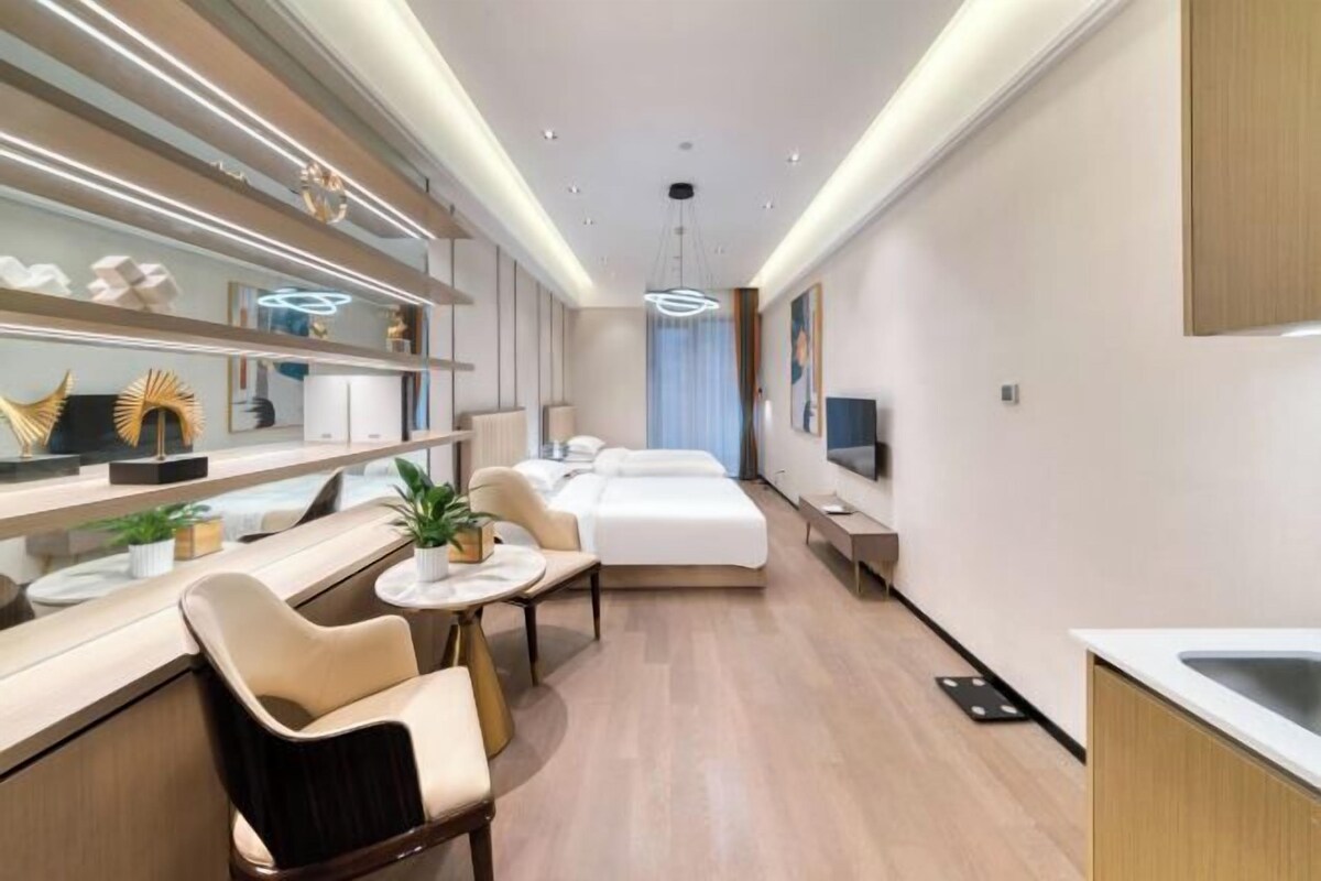 A modern hotel room with a bed, bedside table, chair, and a small dining area.
