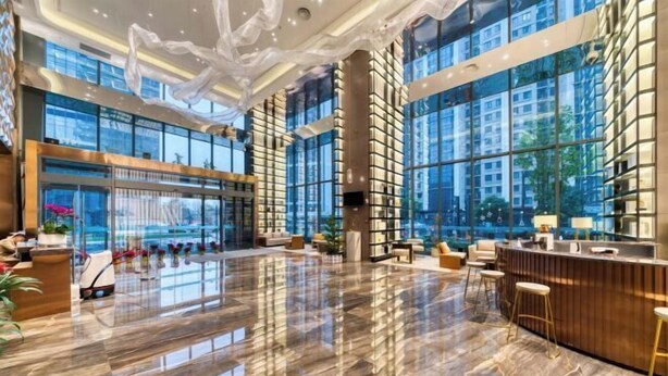 A spacious lobby with a polished marble floor, large windows offering views of the city, and a reception area with a wooden counter and bar stools. - Humgait Hotel (Hangzhou)