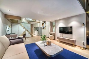 A modern living room with a sofa, a coffee table, a TV, and a staircase leading to a kitchen. - Humgait Hotel (Hangzhou)