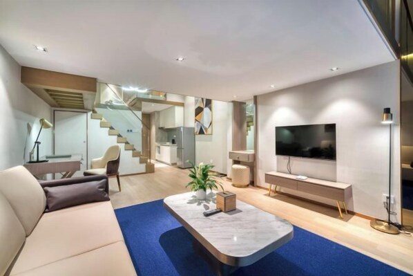 A modern living room with a sofa, a coffee table, a TV, and a staircase leading to a kitchen. - Humgait Hotel (Hangzhou)