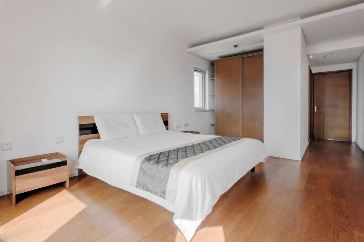Une chambre moderne avec un lit, des tables de chevet en bois, une armoire et une fenêtre.