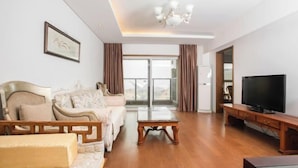 A spacious living room with a sofa, a coffee table, a TV, and a large window with curtains.