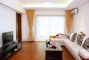 A living room with a sofa, a coffee table with flowers, a TV, and a window with curtains. - Yimei Boutique Hotel (Golden Beach Impression) (Qingdao)