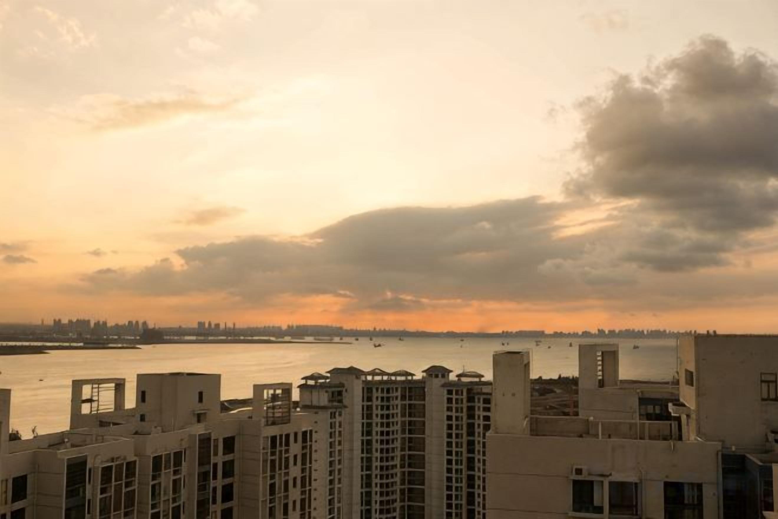 A high-rise building with multiple balconies overlooking a body of water during sunset.