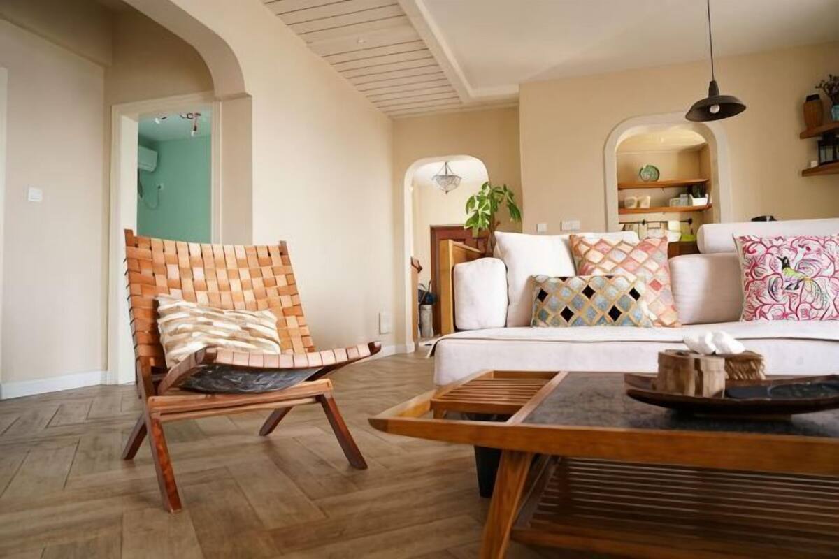 Una sala de estar con una silla de madera, un sofá, una mesa de centro y una lámpara colgante.