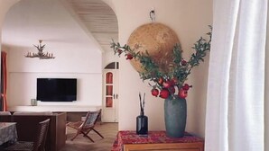 Een woonkamer met een televisie, een eethoek en een grote vaas met bloemen.