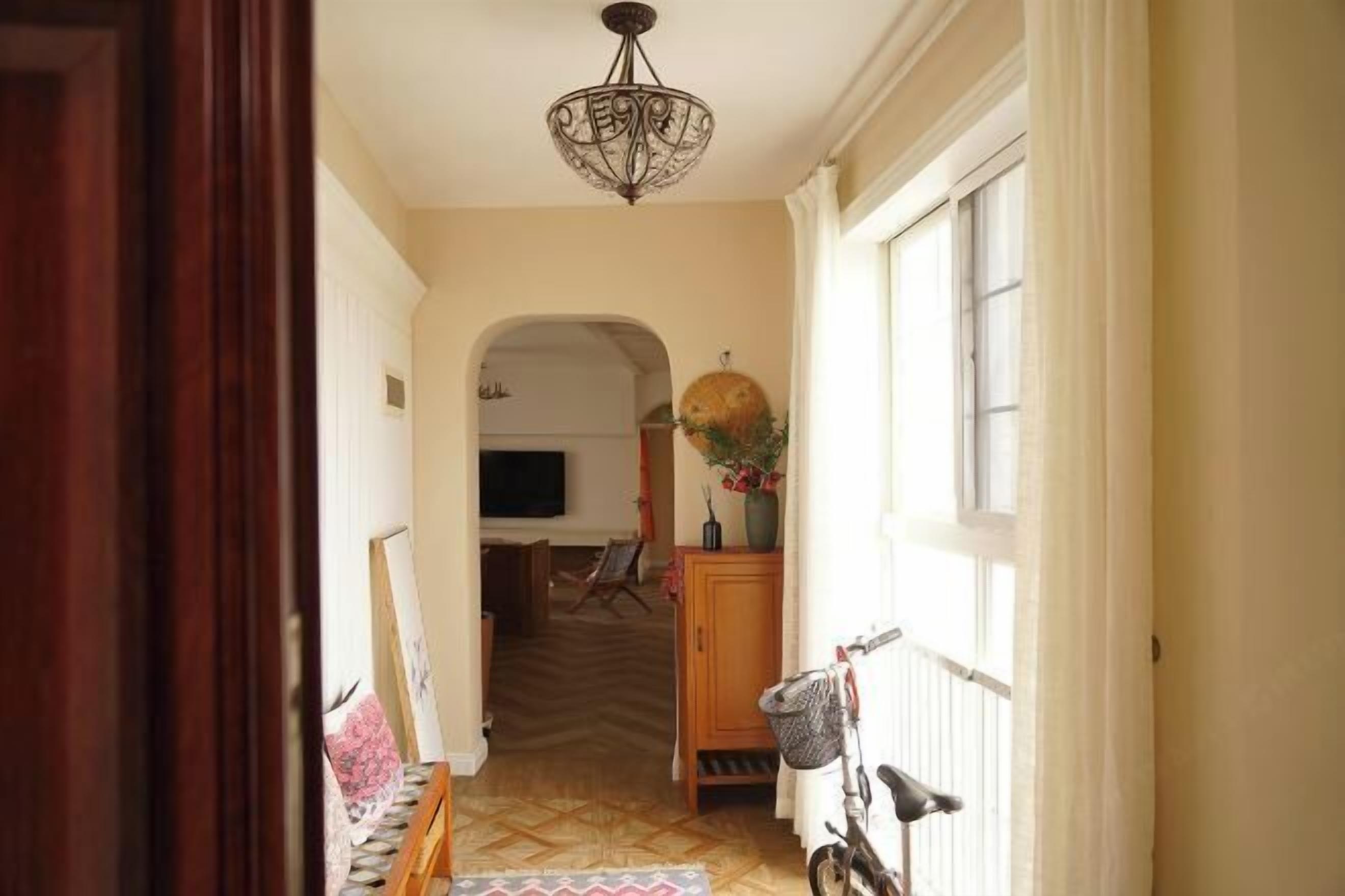 Un pasillo con una puerta de madera, una bicicleta, un televisor montado en la pared y un tapete estampado.