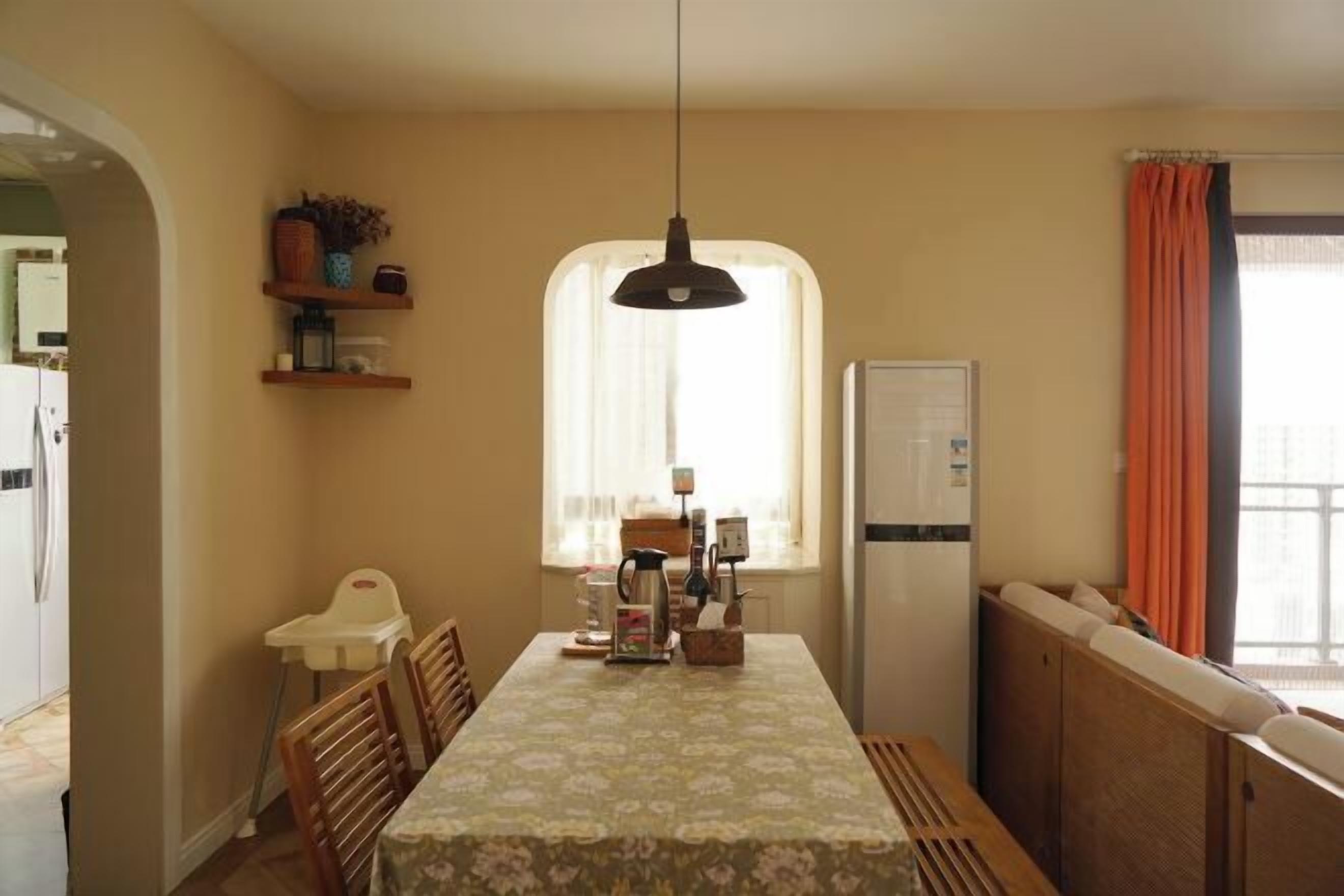 A compact kitchen with a dining table, chairs, a hanging light, and a window with curtains.