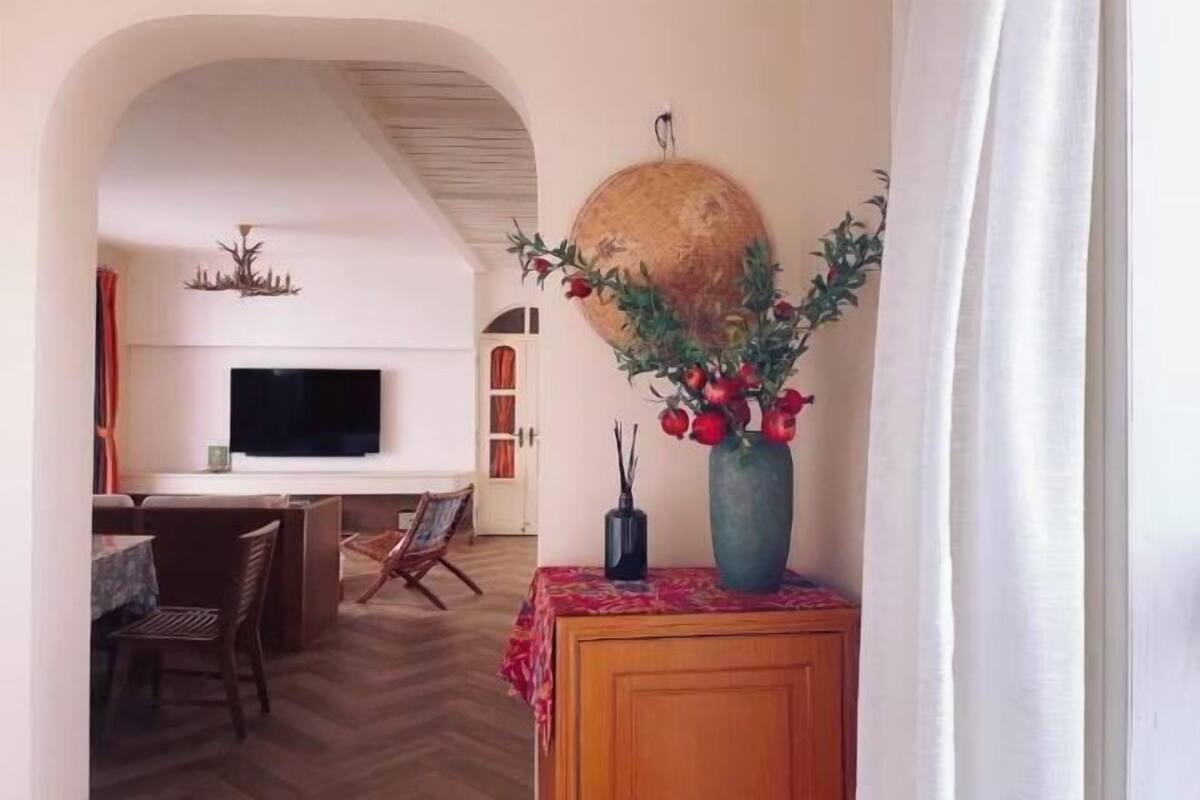 Una sala de estar con televisor, un comedor con sillas, un mueble de madera con un jarrón y un gran globo decorativo en la pared.
