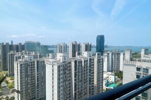 Un edificio residencial alto con varios balcones, cielo despejado y una vista distante de una masa de agua.