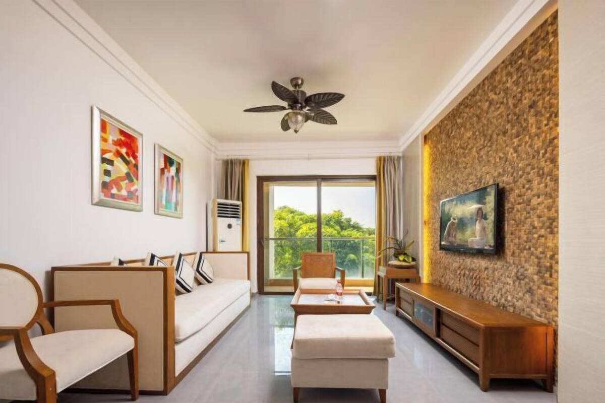 Een moderne woonkamer met een bank, stoelen, een salontafel en een televisie aan een stenen muur.