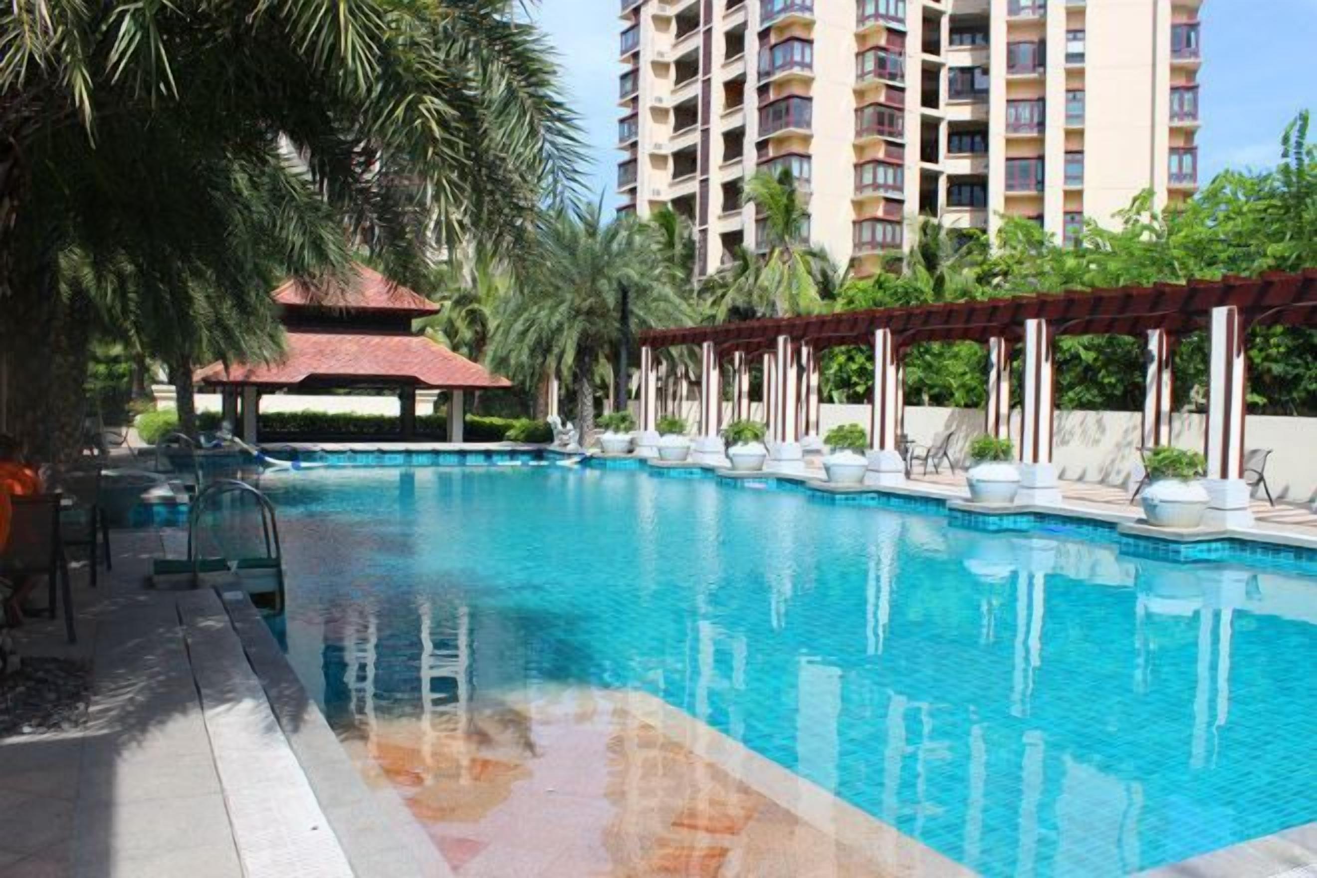 A swimming pool with a pergola, lounge chairs, and a tall building in the background.