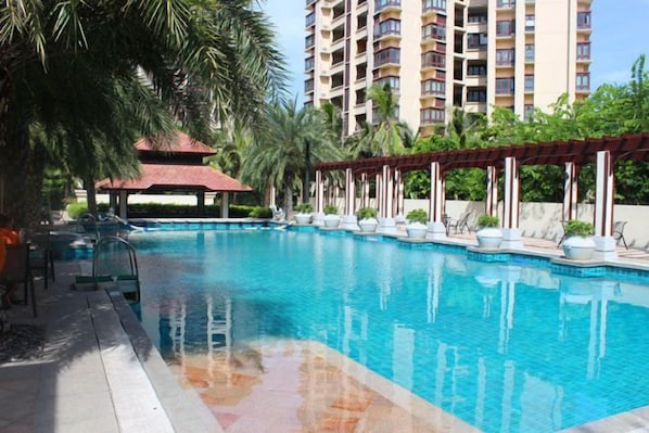 Una piscina con una pérgola, sillas de descanso y un edificio alto al fondo.