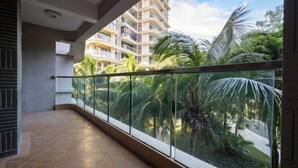 A balcony with a glass railing overlooking a residential area with palm trees and a multi-story building in the background. - Lingshui Ocean Heart Hotel (Clear Water Bay) (Lingshui)