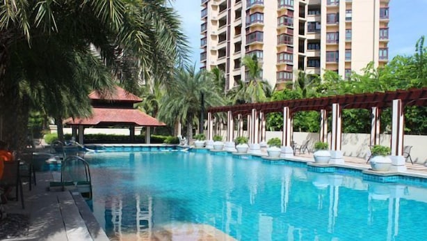 A swimming pool with lounge chairs and a gazebo, surrounded by palm trees and a tall building in the background. - Lingshui Ocean Heart Hotel (Clear Water Bay) (Lingshui)