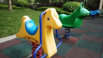 A playground with a yellow and green seesaw and a blue tricycle.