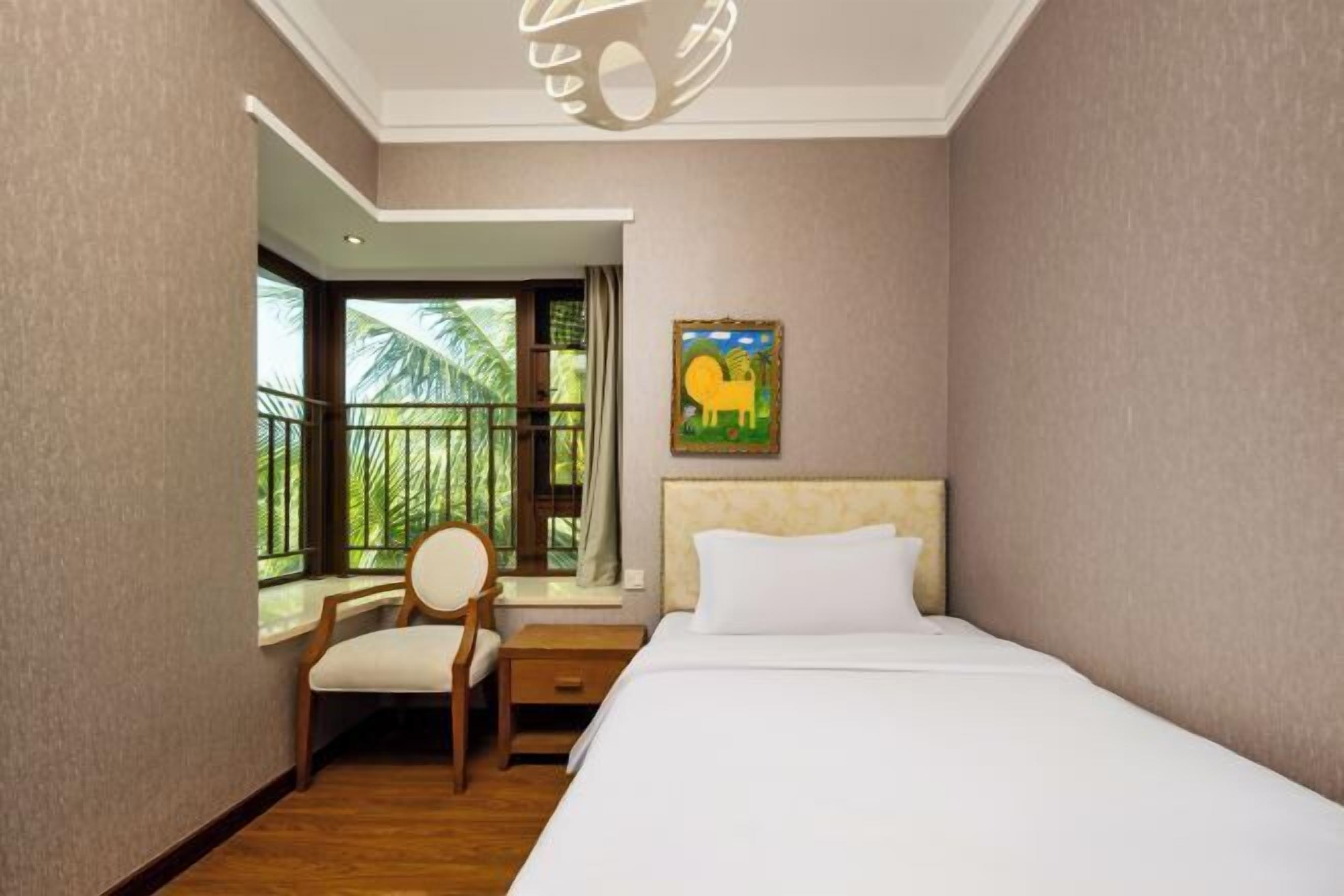 Quarto de hotel com uma cama, uma cadeira, uma mesinha de cabeceira, uma janela com vista para palmeiras e um quadro na parede.