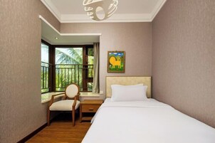 Una habitación de hotel con cama, una silla, una mesita de noche, una ventana con vista a palmeras y un cuadro en la pared.