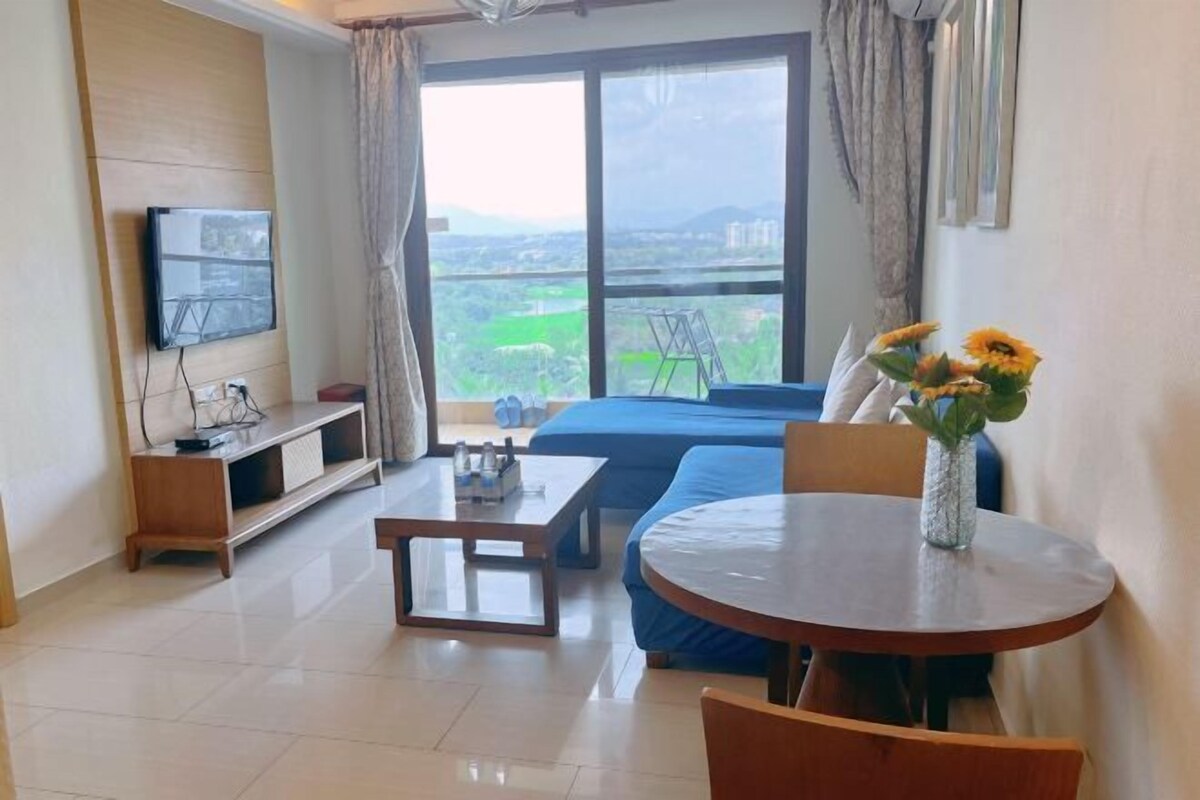 Habitación de hotel con una ventana grande, una cama, un televisor montado en la pared, una mesita y una silla.