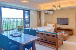 Habitación de hotel con cama, televisión, mesa de comedor con sillas y balcón con vistas a zonas verdes.