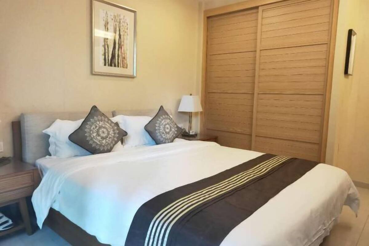 Een netjes opgemaakt bed met een zwart-witte strepen dekbed, twee sierkussens, een bedlampje en een houten garderobe.