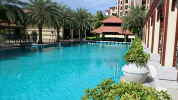 A swimming pool with a tiled deck, palm trees, and a building with a red roof.