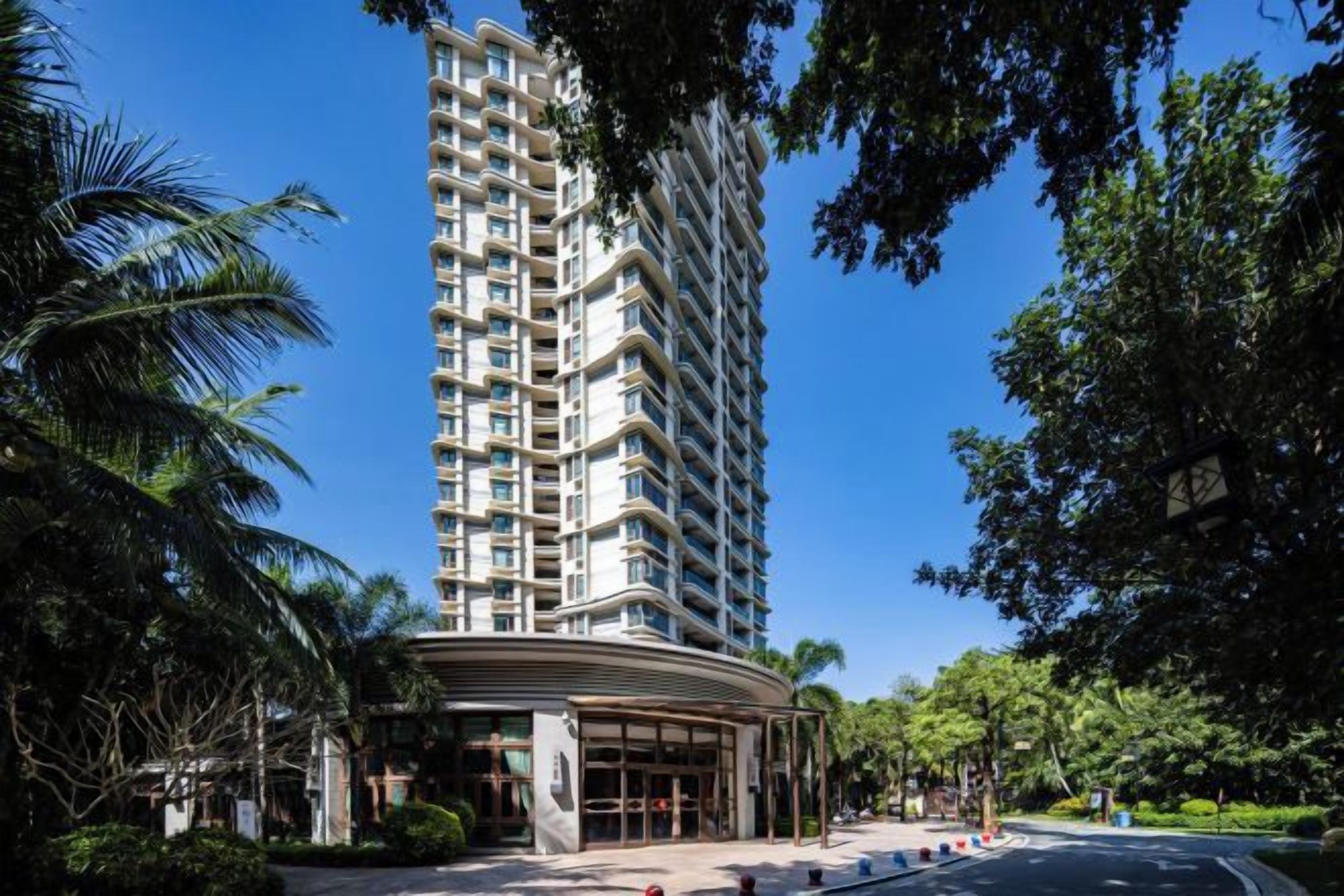 A high-rise hotel with a curved entrance, surrounded by lush greenery and palm trees.