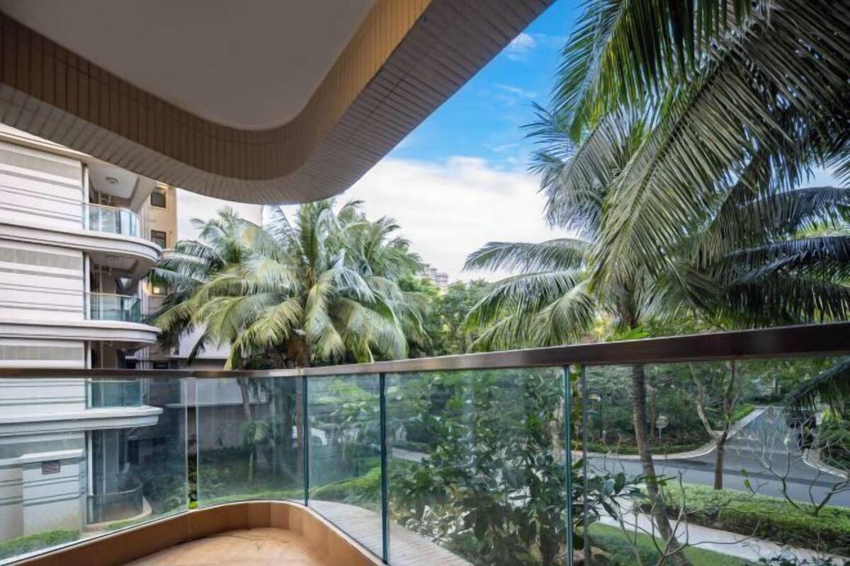 Een modern gebouw met een gebogen balkon dat uitkijkt over een weelderige tuin met palmbomen.