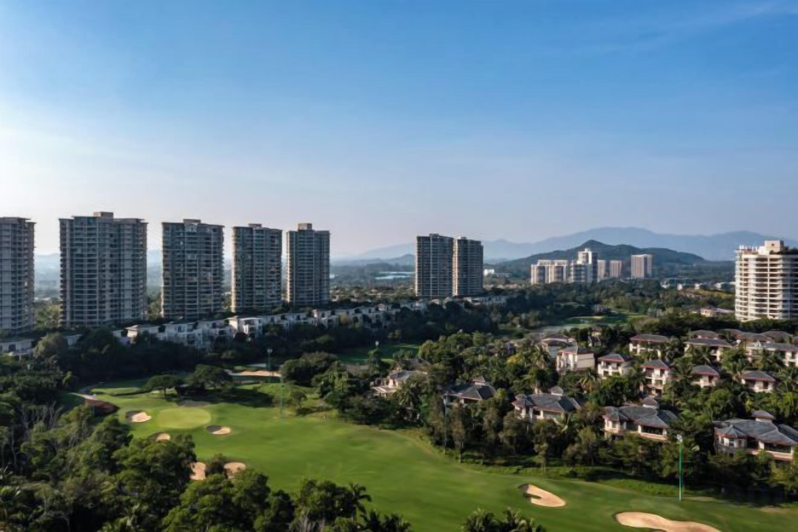 A residential area with high-rise buildings, a golf course, and a hilly landscape in the background.